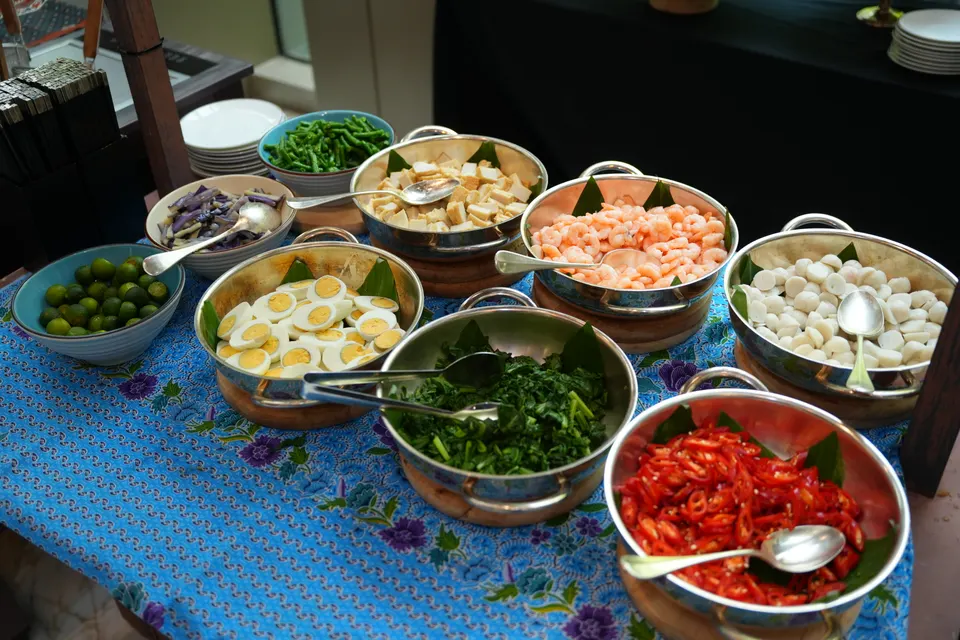 A buffet of local dishes in brass bowls on a batik cloth