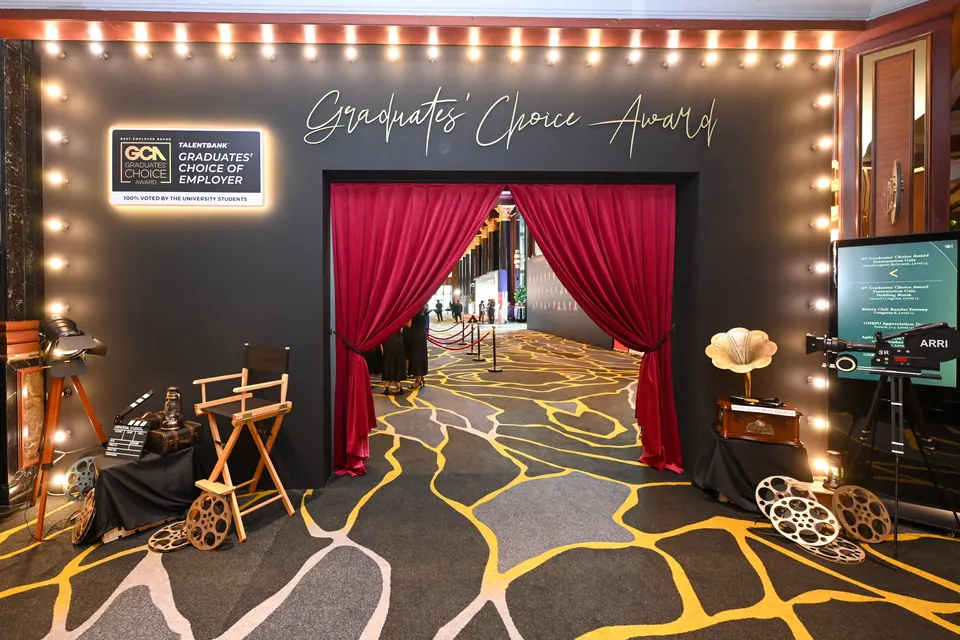 A film-set entrance with a red curtain, bulb lights, a director's chair and film props at a gala