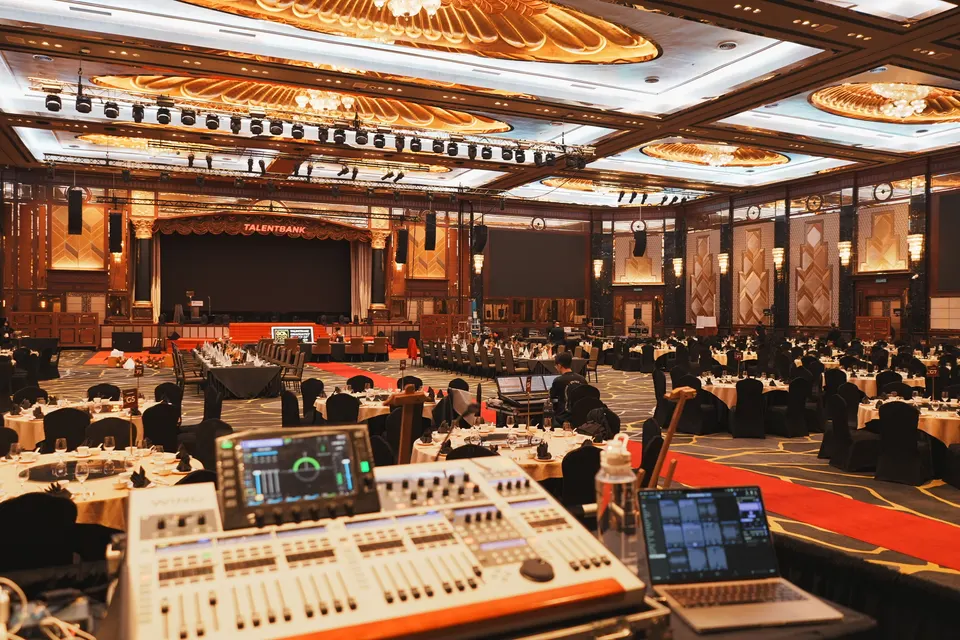 The production desk at the back of a ballroom, with the tables set and the stage ahead
