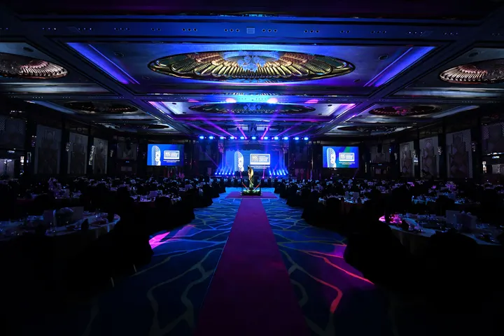 A ballroom lit in blue, with a long aisle carpet leading to the stage