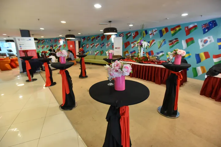 A reception area with cocktail tables dressed in black and red, pink flowers and a wall of flags