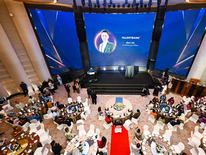 An overhead view of a ballroom with round tables, a red carpet and a large LED screen above the stage
