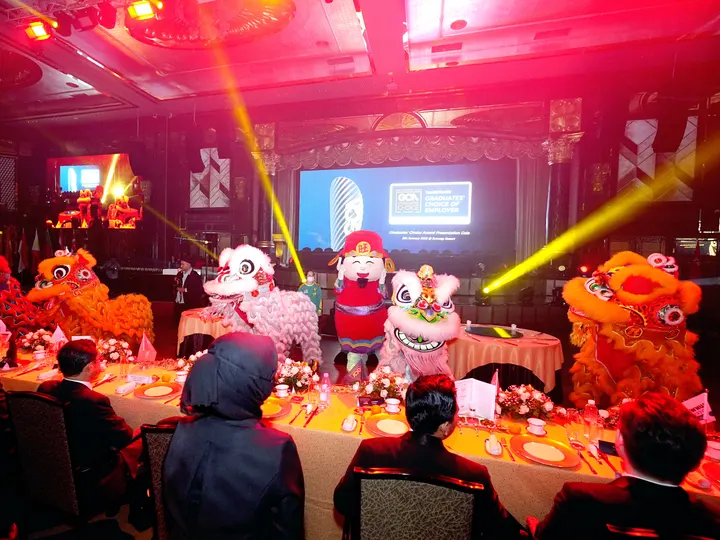 Lion dance performers beside a laid dinner table under red stage lights at the Graduates' Choice Award gala