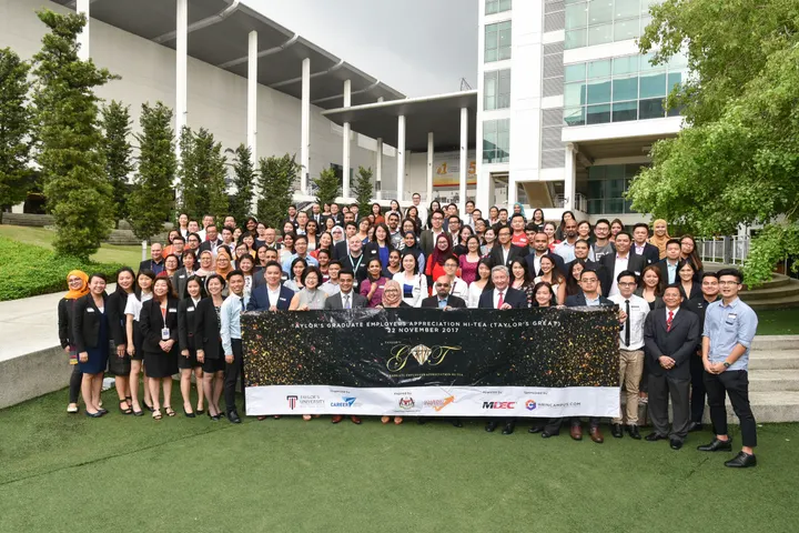 A large group of guests holding a banner on a lawn after a hi-tea