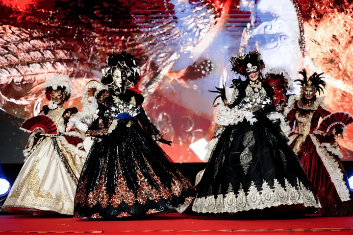 Performers in masquerade costumes and masks on a red stage