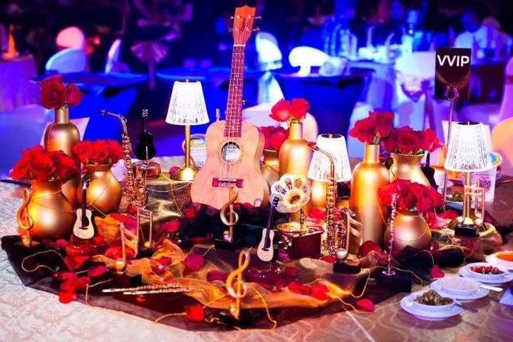 A themed table centrepiece of gold vases, red roses, a ukulele and small musical instruments