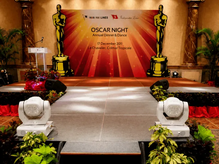A stage dressed for an Oscar Night dinner and dance, with a gold statuette either side of the backdrop