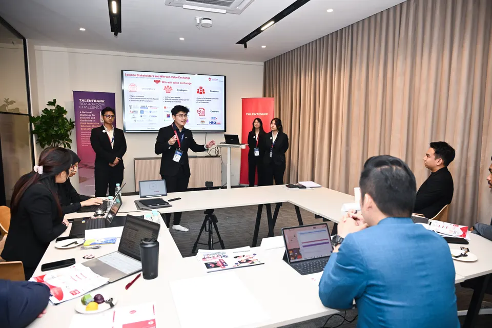 A team presenting a slide while the judges look on from around the table