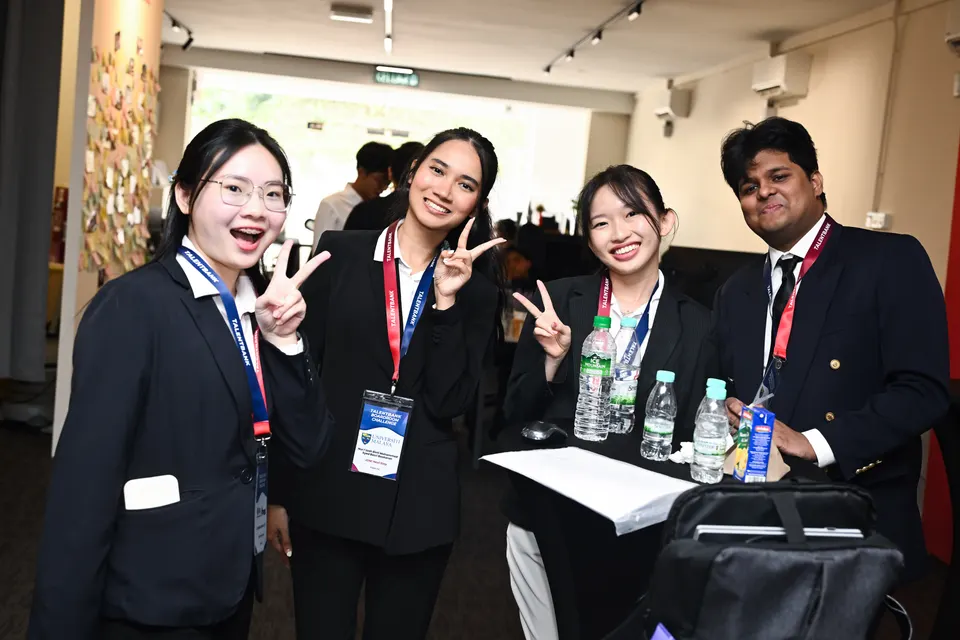 Four students in business attire smiling and making peace signs at the camera
