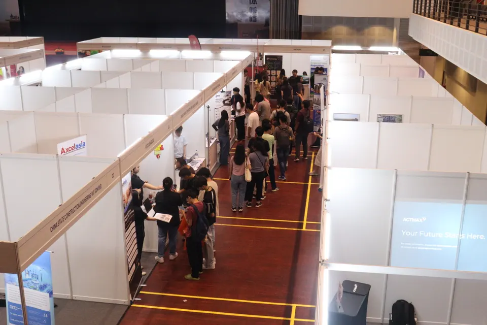 Students filling the aisles between exhibitor booths in a campus career fair hall, seen from above