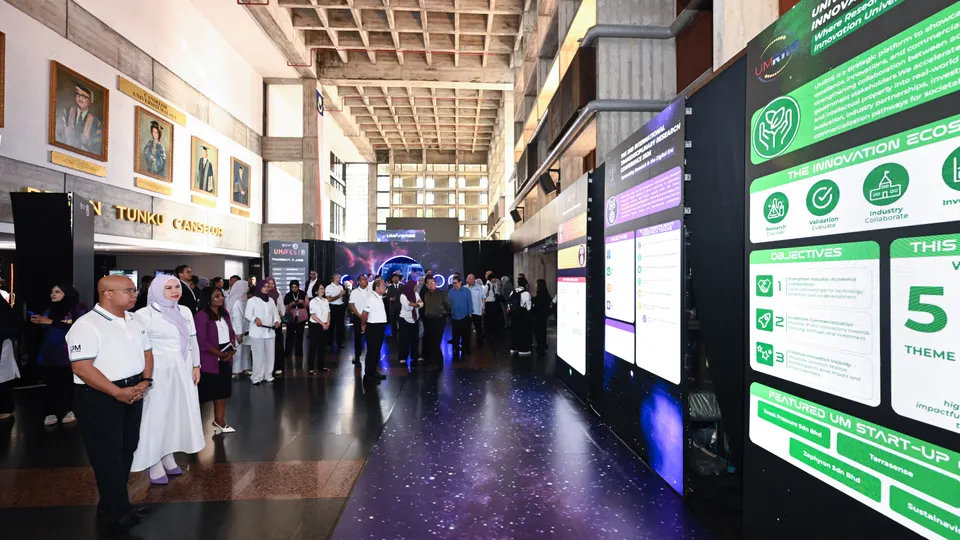 Visitors gathered in a high-ceilinged university hall beside a row of large digital screens