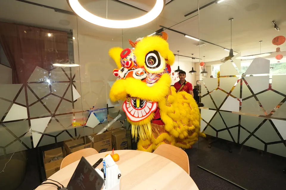 A lion dancer beside a round table in a glass-walled meeting room at the Talentbank office