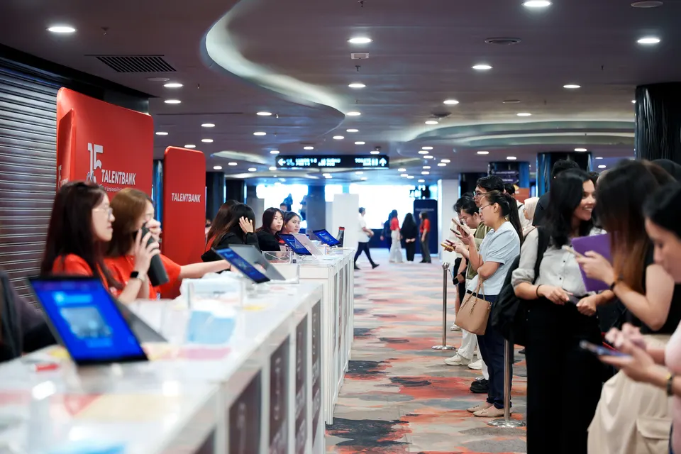 Volunteers in red at the check-in counters of the Talentbank Career Fair, welcoming a queue of visitors