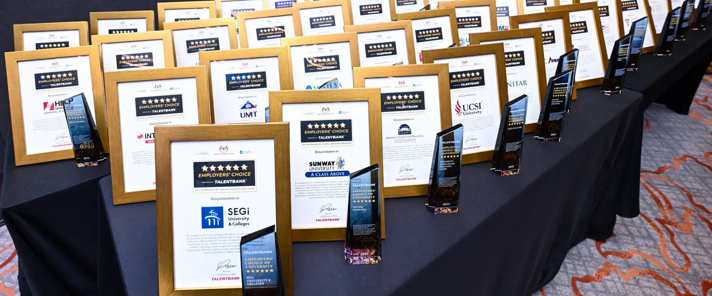Rows of framed Employers' Choice certificates, each beside a glass trophy, laid out on a long table