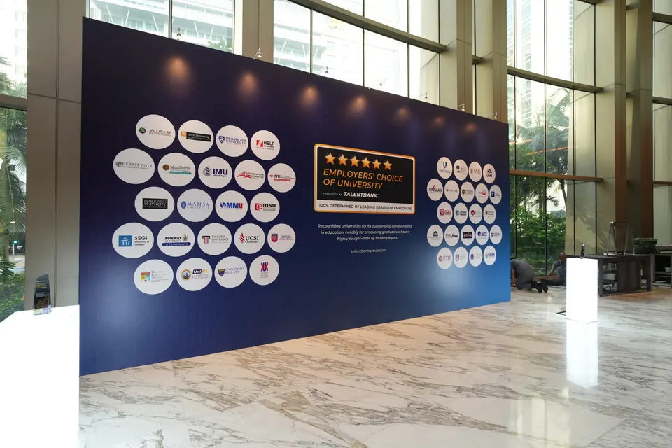 A large navy backdrop of university logos and the Employers' Choice of University mark in a hotel lobby
