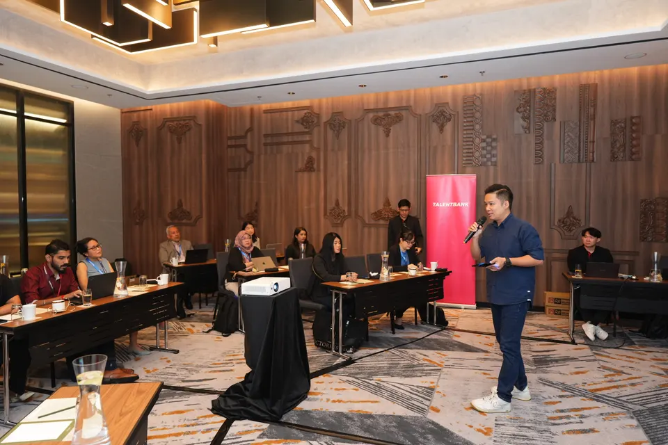A Talentbank speaker addressing a workshop room, with participants seated at long tables facing a projector