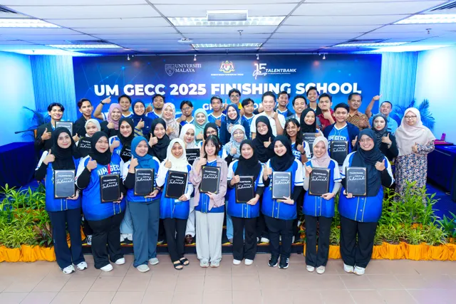 A group of graduates in blue Finishing School jackets holding folders in front of a graduation day backdrop