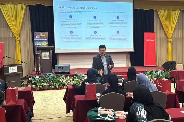 A trainer standing in front of a presentation screen, speaking to learners seated at tables