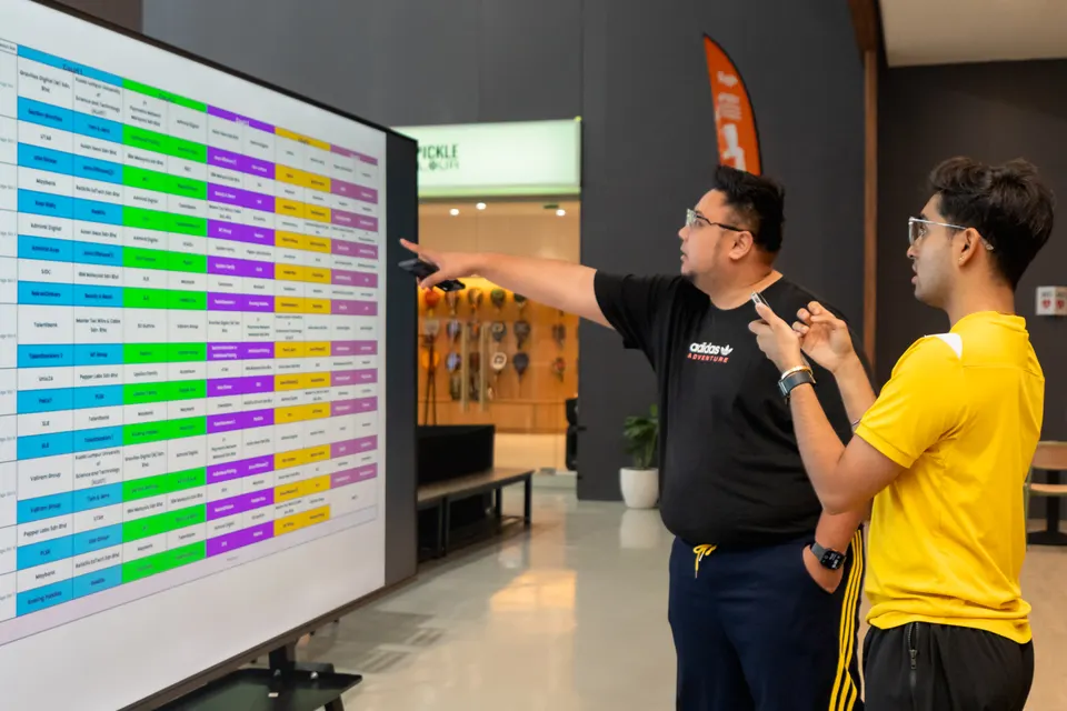 Two players pointing at a colourful fixture board on a large screen