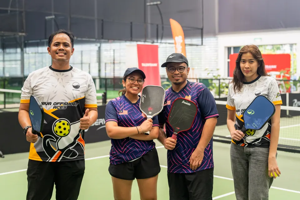 Four players in team jerseys holding their paddles and smiling