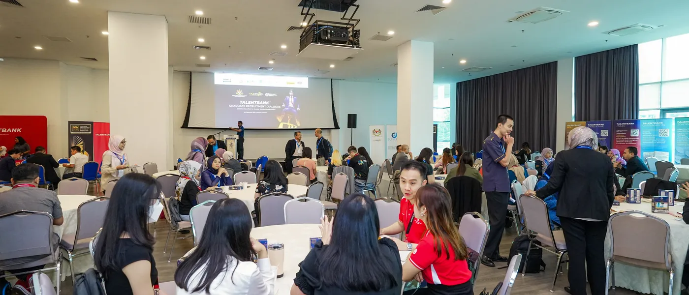 A hall of guests seated at round tables, with a presentation on the screen ahead, at a Talentbank Graduate Recruitment Dialogue