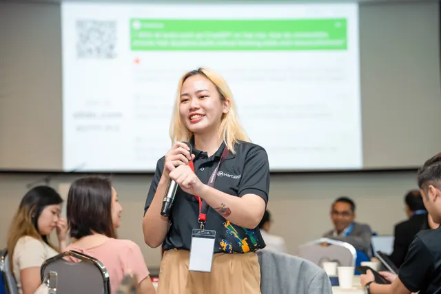 A delegate speaking into a microphone in front of a presentation screen at a Talentbank Graduate Recruitment Dialogue