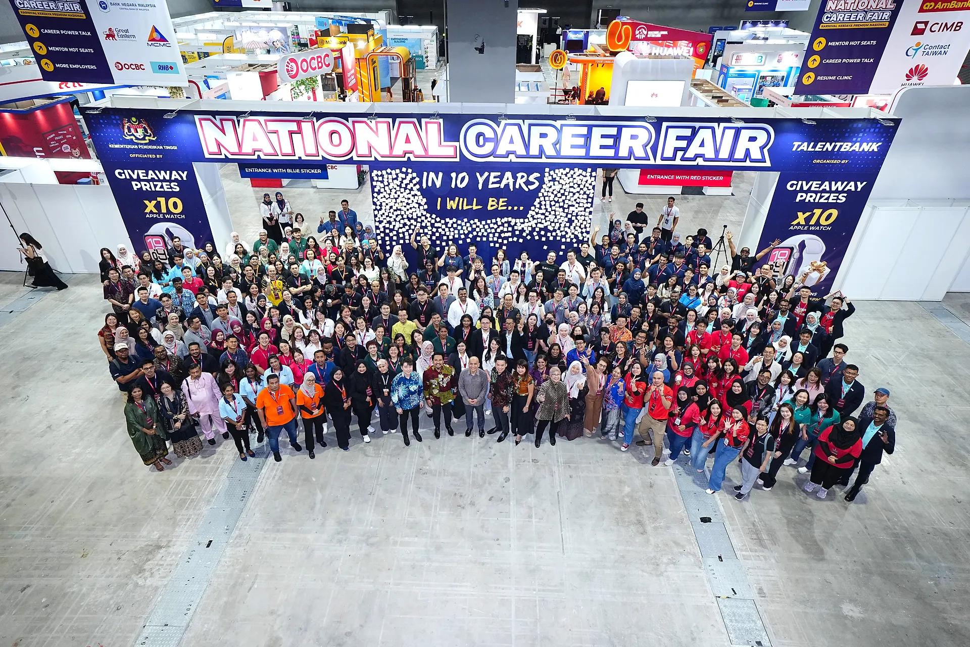 Visitors and crew gathered for a group photo beneath the fair's banner and the wall of employers
