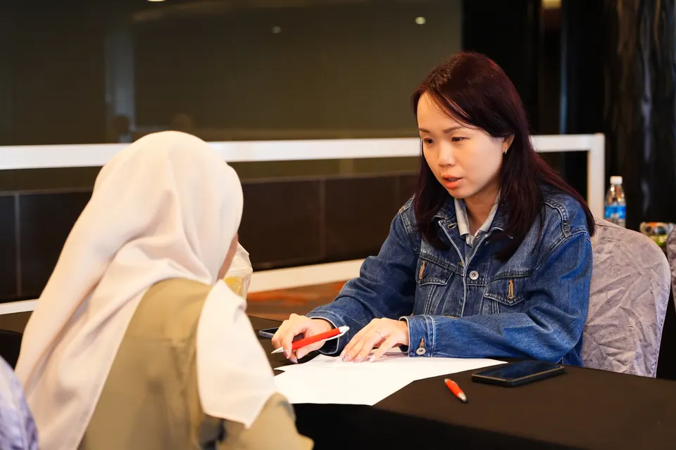 A mentor writing notes while a visitor listens at the Talentbank Career Fair 2025
