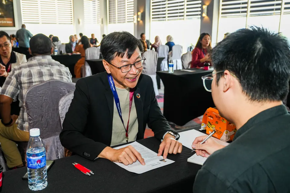 A mentor smiling as he talks with a visitor across a table at the Talentbank Career Fair 2025