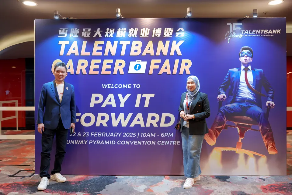 Two people standing beside the Welcome to Pay It Forward backdrop at the Talentbank Career Fair 2025